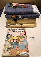 Stack of folded Charlie Brown bedding bedspreads with a Charlie Brown Dictionary book in front