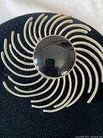 Close-up front view of the brooch showing the polished black onyx center and curved sterling silver rods in a sunburst pattern.