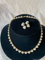 Full view of the gold-tone heart necklace and matching stud earrings on black display stand showing design and style.