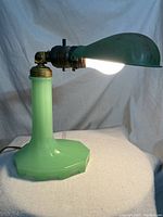 Front angle view of the lamp lit, showing the jadeite glass base and patina metal tilting shade.