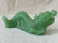 Side profile of the smooth, green jadeite jade Asian dragon figurine displaying detailed texturing and scale carving along the body and curved tail.