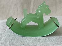 Side view of the green jadeite jade rocking terrier dog figurine showing dog details and curved rocker base with metal pins.