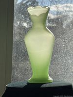 Vintage jadeite vase shown backlit to highlight its translucent light green glass and shape details.