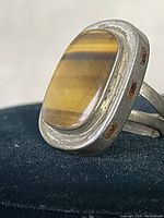 Close-up angled view of the vintage sterling silver ring with tiger eye stone resting on a black background, showing the stone's color and silver setting details.