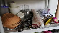 Shelf with various kitchenware including clay baker, Tupperware containers, pie rollers, and metal kitchen tools