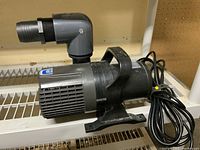 Side view of Oase Living Water fountain pump with right-angle pipe fitting and power cord coiled beside it.