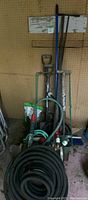 Photo showing multiple garden tools including seedling planter, garden fork, spade, shovel, push broom, hand pump, hose fittings and seed spreader grouped together against pegboard wall