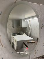 Oval bathroom mirror mounted on wall above a sink and washing machine, showing overall shape and context.