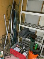 Plant stakes, metal rods, conduit pipes, netting, and plastic containers with small parts in a shelving corner.
