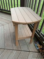 Side view of light brown composite side table showing slatted top, lower shelf, and leg construction.