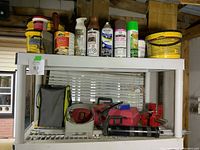 Photo of white shelf with various buckets and cans of patching materials and spray paint; red tool box with Craftsman rotary tool, red vise, grease applicator, flexible snake, calipers in wooden box, Ryobi tool bag