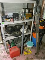Photo of shelving unit with items on and around it, including wheels, buckets, power cords, and tools.