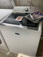 White Maytag washer with black textured glass top and control panel with dial and buttons