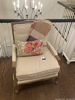 Front view of beige upholstered accent chair with decorative pillow and striped blanket draped over backrest.