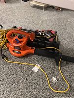 Orange Black and Decker electric leaf blower model BV3600 with yellow extension cord and foldable hand truck on floor.
