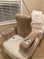 Brookstone massage chair cushion placed on a white striped armchair showing front view with cup holder and control buttons visible.