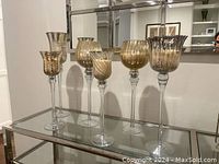 Full view of all six mercury glass candle holders with candles on a glass console table with mirror in background