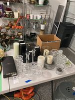 Overview of various candles and candleholders on a white table, including boxed items and pillar candles.