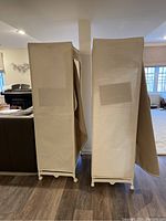 Photo of two beige fabric storage closets side by side on their white wheeled bases, closed fronts.