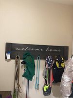 Front view of the wooden coat rack mounted on a wall with several items hanging on hooks to show size and function. The rack has the text 'welcome home' painted in white.