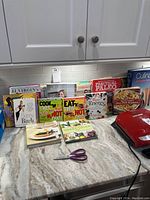 Photo showing full collection of cookbooks and diet books arranged in a row on countertop.