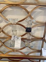 Pair of tall clear crystal candlesticks with faceted square bases and tops, labeled Precious Home, around 10 inches tall, placed on a shelf against decorative gold metal background.