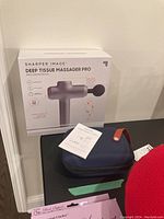 Sharper Image Deep Tissue Massager Pro box standing upright with Youmay device in navy case in front and instruction manual visible.