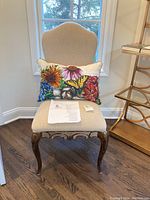 Front view of beige upholstered desk chair with curved wooden legs and floral butterfly pillow on seat