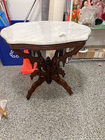 Front view of the marble top pedestal table showing the white marble surface and wooden carved pedestal and legs.