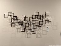 Full front view of the metal wall sculpture showing the interconnected square frames against a white wall.