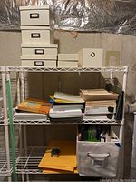 Full view of metal shelving unit with various storage boxes, organizers, binders, file folders, and padded envelopes arranged on multiple shelves.
