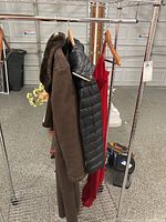 Full view of women's clothing hanging on rack, including brown fur-collared coat, black quilted jacket, and red dress.