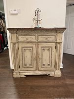 Front view of worn Paradigm solid wood dresser with two drawers and two cabinet doors, detailed carved panels, distressed paint.