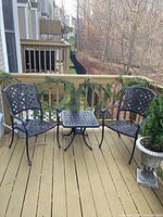 Photo of wrought aluminum patio table and two matching chairs on wooden deck with natural background.