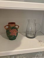 Photo showing Roseville water lily vase and one clear glass pitcher side by side on shelf