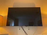 Front view of Samsung 40-inch flat-screen TV mounted on the wall with cables hanging below, showing the screen off and in good condition.