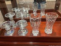 Overview of the four clear pillar candle holders and two crystal vases placed on a wooden surface with mirror background.