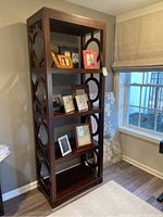 Full front view of wooden shelving unit with photo frames on shelves next to window and wall.