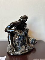 Front view of the dark-colored ceramic statue of a man playing drums, showing detailed facial expression and the drum surface.