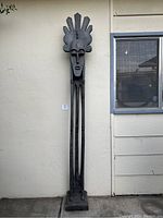 Full-height view of the tall African wooden statue leaning against a wall near window.