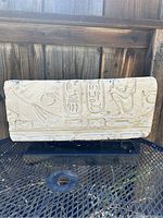 Front view of rectangular Egyptian painted cement art piece with hieroglyphics and figures, mounted on black base, showing minor wear.