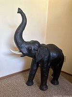 Large black leather elephant statue standing on carpeted floor with trunk raised.