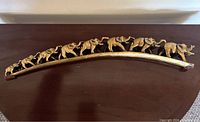 Full view of the curved vintage gold painted elephant sculpture showing nine elephants walking in line.