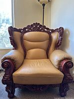 Front view of vintage armchair showing tan leather upholstery and ornate carved wood frame.