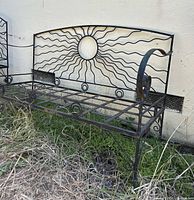 Side view of the vintage wrought iron bench showing scroll armrest and sun rays design on backrest