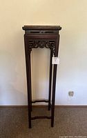 Full view of tall carved rosewood pedestal against wall