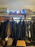 Photo shows rack filled with vintage clothes including jackets, coats, packs, baskets, and stools visible below rack