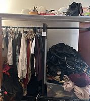 Photo showing vintage clothing items hung on metal rack including jackets, shirts, and tops in various colors and fabrics