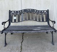 Front view of the outdoor bench showing metal frame with wooden slats and floral design on backrest.