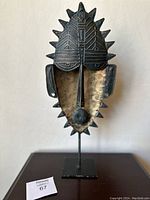 Front view of the vintage Philippines tribal mask showing carved detailed top, spikes around the oval shape, and nose-like protrusion, mounted on a black metal stand
